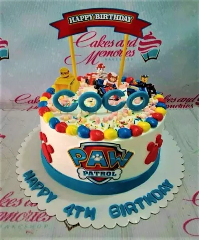A white 1-tier cake themed around Paw Patrol, featuring character printouts, a "Happy Birthday" banner, and blue icing borders. A white 1-tier cake themed around Paw Patrol, featuring character printouts, a "Happy Birthday" banner, and blue icing borders.