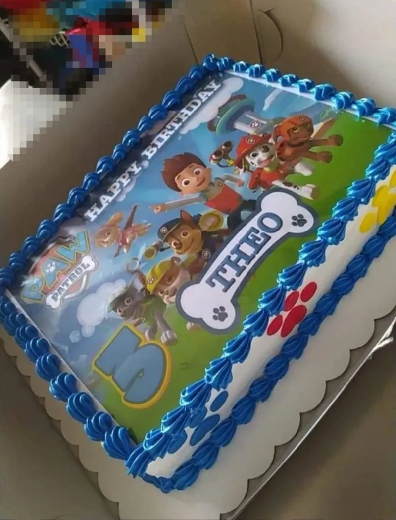 A white rectangle Paw Patrol cake, with printed characters, a blue '3', blue icing borders, and paw prints. A white rectangle Paw Patrol cake, with printed characters, a blue '3', blue icing borders, and paw prints.