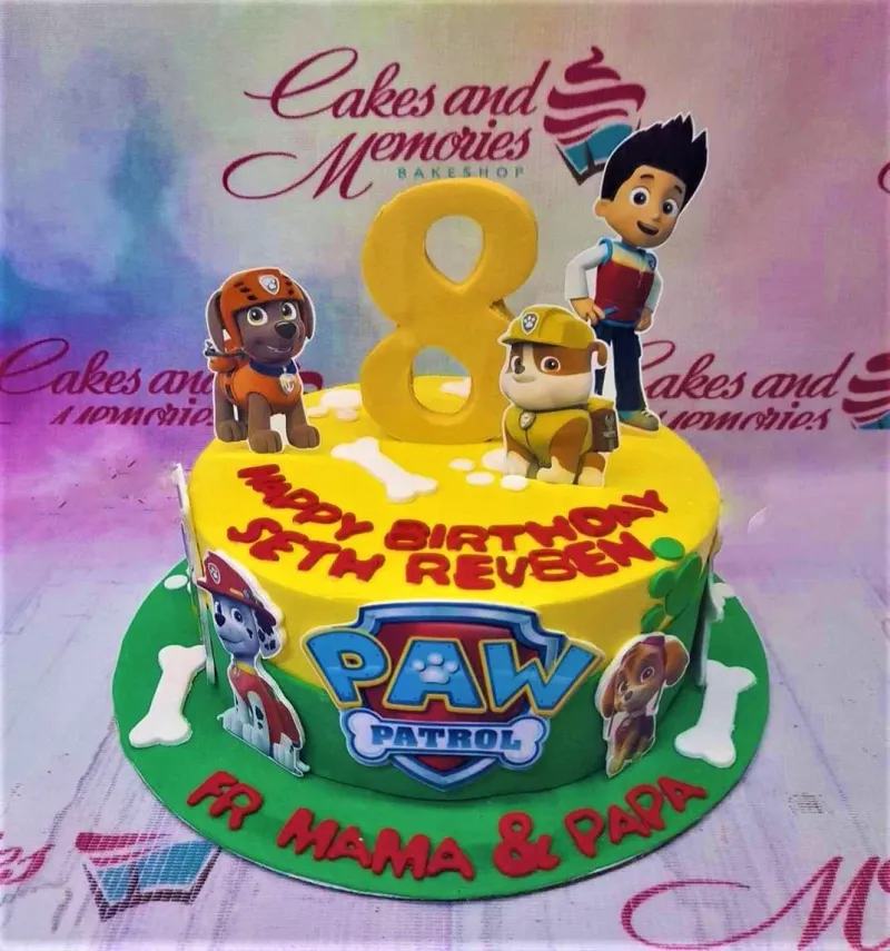 A yellow and green 1-tier Paw Patrol cake, featuring Ryder, pup printouts, a large yellow 8, white bones, and green paw prints. A yellow and green 1-tier Paw Patrol cake, featuring Ryder, pup printouts, a large yellow 8, white bones, and green paw prints.