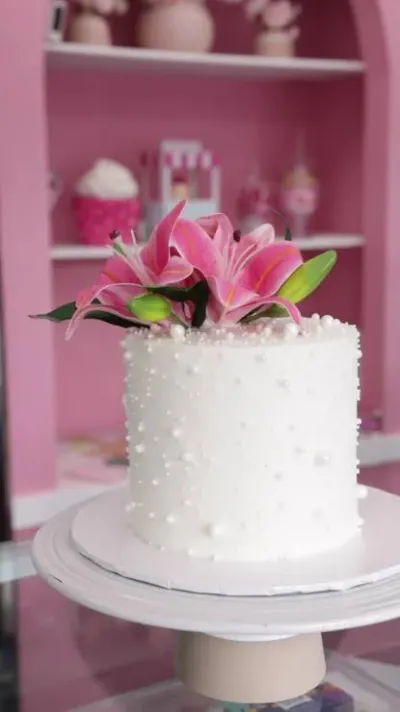 White 1-tier cake with smooth soft icing, three pink and white lily flowers, and scattered white sugar pearls White 1-tier cake with smooth soft icing, three pink and white lily flowers, and scattered white sugar pearls