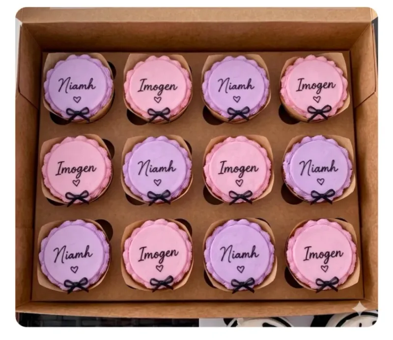 Lavender and pink cupcakes in a box with piped frosting borders, black script names, and tiny black ribbon bows Lavender and pink cupcakes in a box with piped frosting borders, black script names, and tiny black ribbon bows