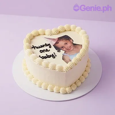 White heart-shaped cake with soft icing, an edible photo print, black piped text, and black ribbon bow accents White heart-shaped cake with soft icing, an edible photo print, black piped text, and black ribbon bow accents