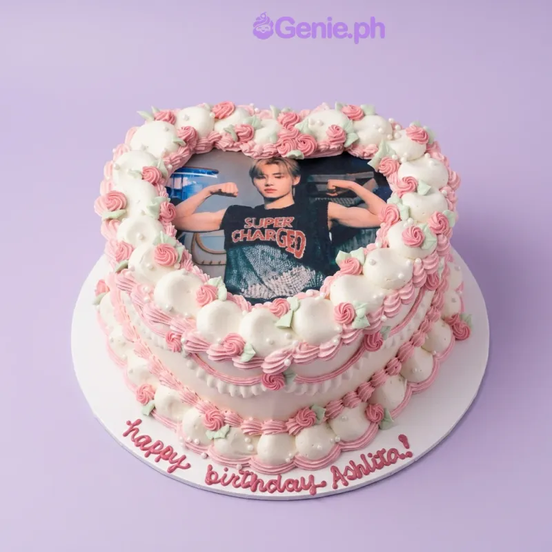 Heart-shaped white cake with a photo print in the center surrounded by pink icing roses and green leaves Heart-shaped white cake with a photo print in the center surrounded by pink icing roses and green leaves