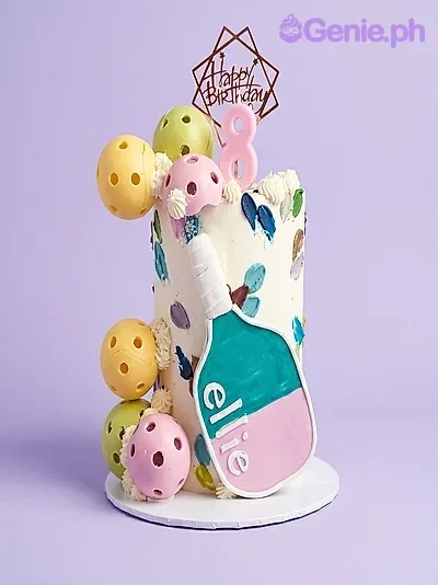 White single tier cake with a pickleball paddle topper, pink number 8 candle, and colorful pickleball spheres White single tier cake with a pickleball paddle topper, pink number 8 candle, and colorful pickleball spheres