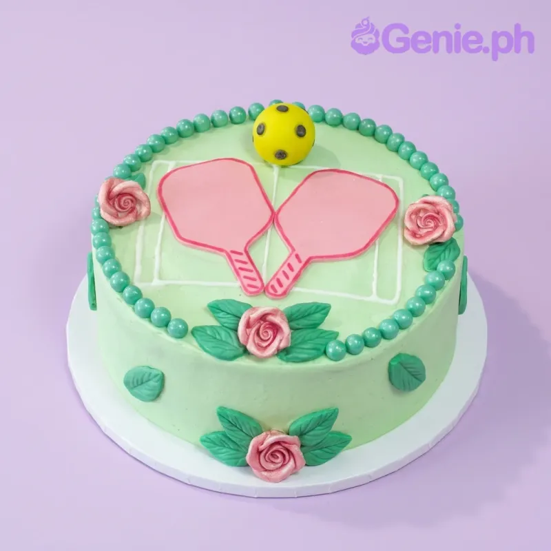 A light green 1 Tier cake themed around Pickleball, featuring pink paddles, a yellow ball, pink icing roses, and white court lines. A light green 1 Tier cake themed around Pickleball, featuring pink paddles, a yellow ball, pink icing roses, and white court lines.