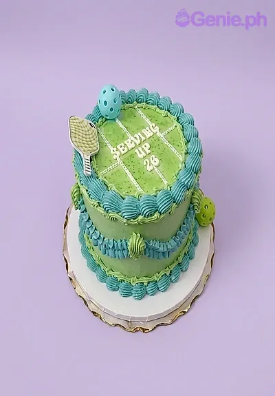 Green single tier pickleball themed cake with teal piped borders and a pickleball paddle topper Green single tier pickleball themed cake with teal piped borders and a pickleball paddle topper