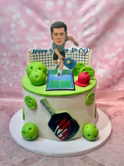 White 1-tier cake with smooth soft icing, Pickleball theme, caricature man printout, and net plaque White 1-tier cake with smooth soft icing, Pickleball theme, caricature man printout, and net plaque