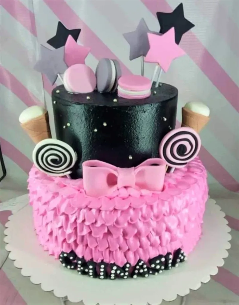 Two-tier pink and black cake with pink icing ruffles, black top tier, pink bow, macarons, and star toppers. Two-tier pink and black cake with pink icing ruffles, black top tier, pink bow, macarons, and star toppers.