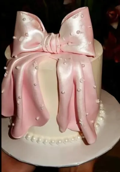 A white and pink 1-tier cake themed around Pink Bow, featuring a large pink fondant bow and white pearl accents. A white and pink 1-tier cake themed around Pink Bow, featuring a large pink fondant bow and white pearl accents.