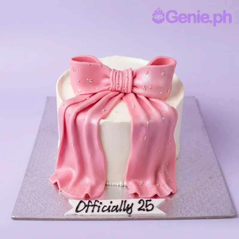 A white and pink single tier cake themed around a Pink Bow, featuring a large pink fondant bow and white edible pearls with a text banner. A white and pink single tier cake themed around a Pink Bow, featuring a large pink fondant bow and white edible pearls with a text banner.