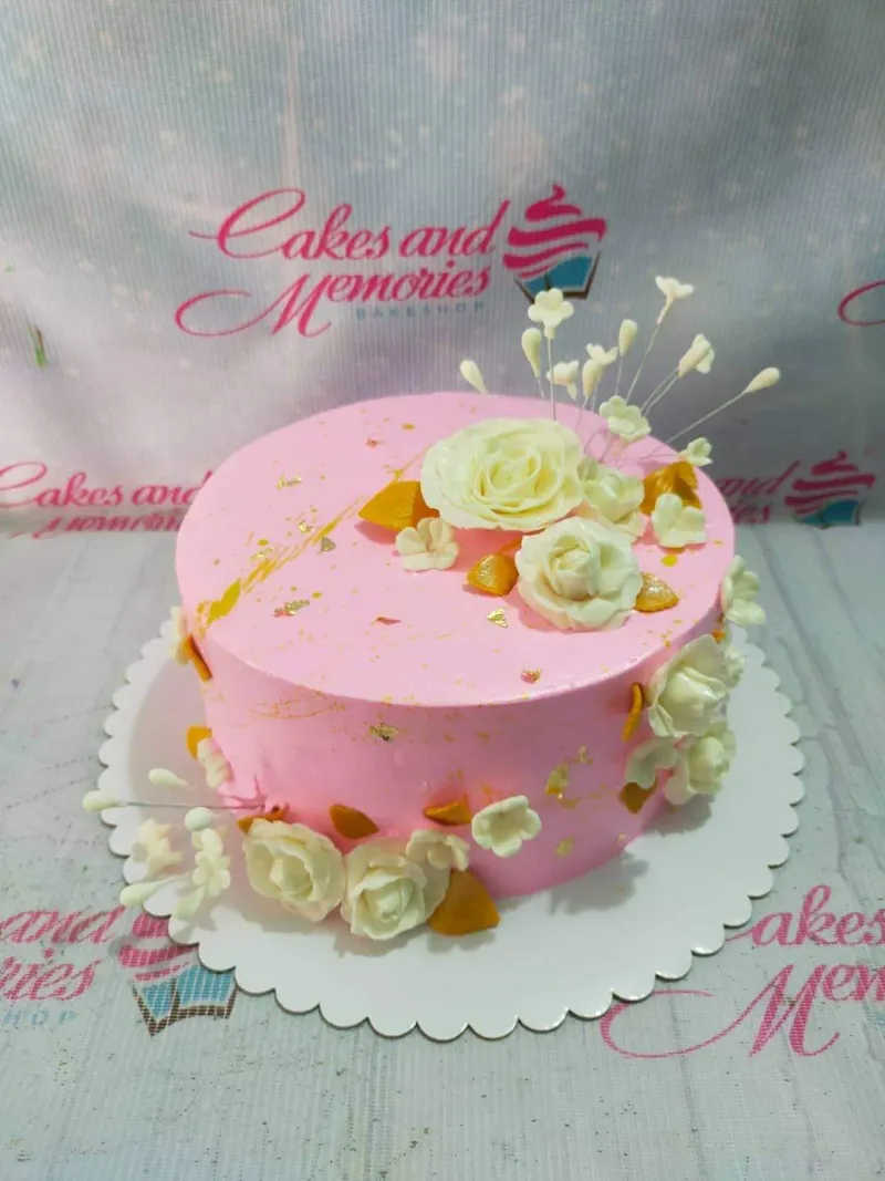 A pink, white, and gold 1 Tier cake themed around Pink Floral, featuring white gumpaste roses, white blossoms, and gold leaf accents. A pink, white, and gold 1 Tier cake themed around Pink Floral, featuring white gumpaste roses, white blossoms, and gold leaf accents.