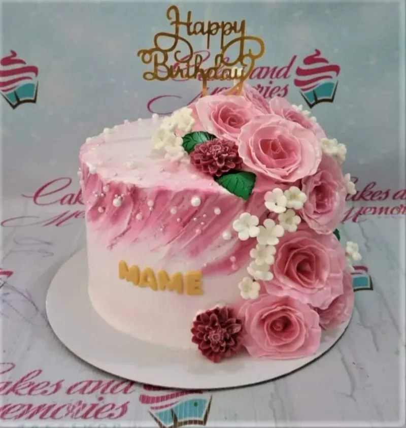 A pink and white 1-tier cake, Pink Floral themed, featuring a gold Happy Birthday topper, pink roses, white blossoms, and 'MAME' lettering. A pink and white 1-tier cake, Pink Floral themed, featuring a gold Happy Birthday topper, pink roses, white blossoms, and 'MAME' lettering.