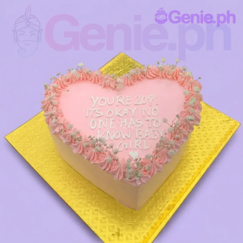 A pink and white 1 tier cake, heart-shaped, featuring a humorous white icing message, pink rosettes, and white baby's breath. A pink and white 1 tier cake, heart-shaped, featuring a humorous white icing message, pink rosettes, and white baby's breath.