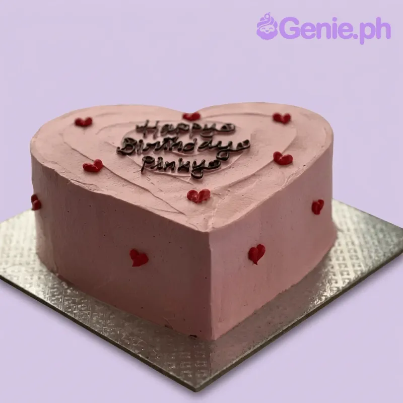 A pink heart-shaped 1-tier cake with a minimalist heart theme, featuring small red icing hearts and a black piped message. A pink heart-shaped 1-tier cake with a minimalist heart theme, featuring small red icing hearts and a black piped message.