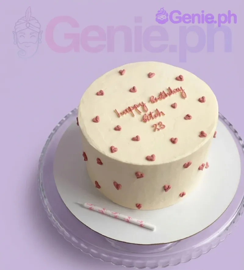 A minimalist ivory 1-tier cake with small pink piped icing hearts and a pink text message on top. A minimalist ivory 1-tier cake with small pink piped icing hearts and a pink text message on top.