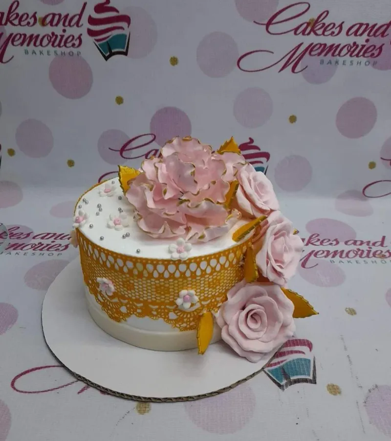 A white 1-tier fondant Pink Peony Floral cake, featuring a large pink peony, gold lace wrap, and silver dragees. A white 1-tier fondant Pink Peony Floral cake, featuring a large pink peony, gold lace wrap, and silver dragees.