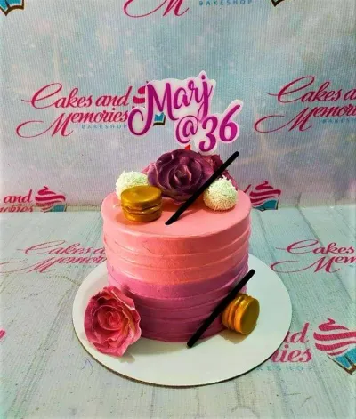 A pink and purple gradient 1-tier cake themed for a birthday, featuring a large purple rose, 'Mary @ 36' topper, and gold macarons. A pink and purple gradient 1-tier cake themed for a birthday, featuring a large purple rose, 'Mary @ 36' topper, and gold macarons.