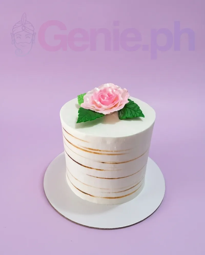 A white 1-tier cake themed Pink Rose Minimalist, featuring a large pink gumpaste rose, green leaves, and gold stripes. A white 1-tier cake themed Pink Rose Minimalist, featuring a large pink gumpaste rose, green leaves, and gold stripes.