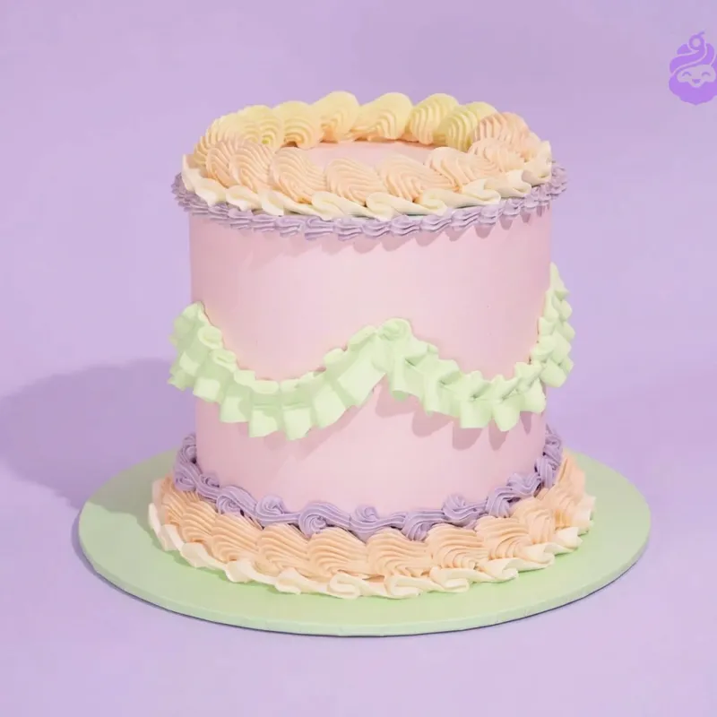 Light pink 1-tier cake with green ruffled icing swag and purple piped borders on a green cake board Light pink 1-tier cake with green ruffled icing swag and purple piped borders on a green cake board