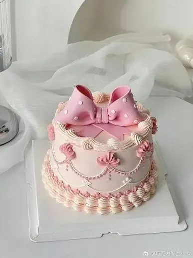 Pink 1-tier cake with soft icing, a pink fondant bow topper, white piped swags, and pearl borders