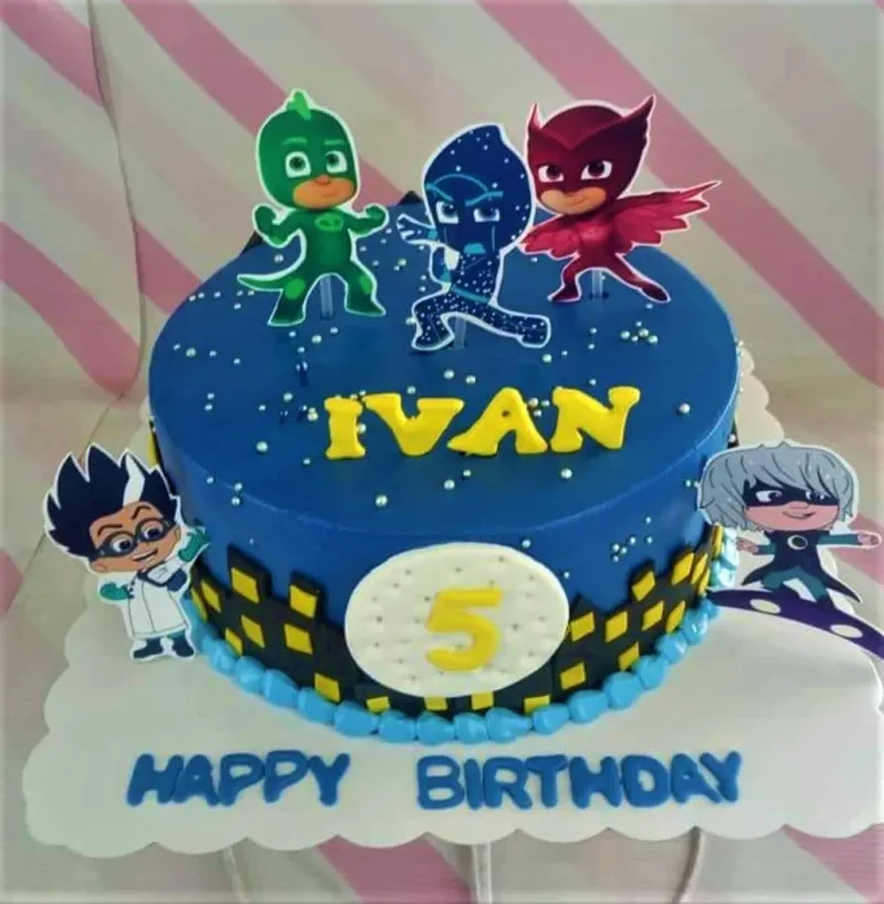 A blue 1-tier PJ Masks cake featuring Gekko, Catboy, Owlette, a black and yellow city skyline, and yellow 'IVAN 5' text. A blue 1-tier PJ Masks cake featuring Gekko, Catboy, Owlette, a black and yellow city skyline, and yellow 'IVAN 5' text.