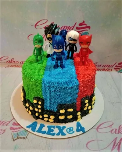 A green, blue, and red 1-tier cake themed around PJ Masks, featuring five PJ Masks character figurines, a black cityscape, and "ALEX @ 4" text. A green, blue, and red 1-tier cake themed around PJ Masks, featuring five PJ Masks character figurines, a black cityscape, and "ALEX @ 4" text.