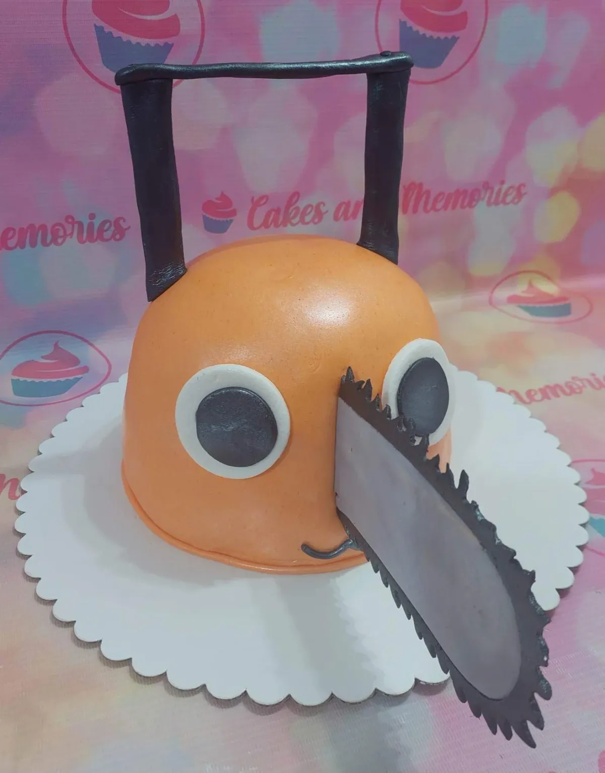 Orange 3D sculpted Chainsaw Man Pochita character cake with a large grey chainsaw blade and black handle. Orange 3D sculpted Chainsaw Man Pochita character cake with a large grey chainsaw blade and black handle.