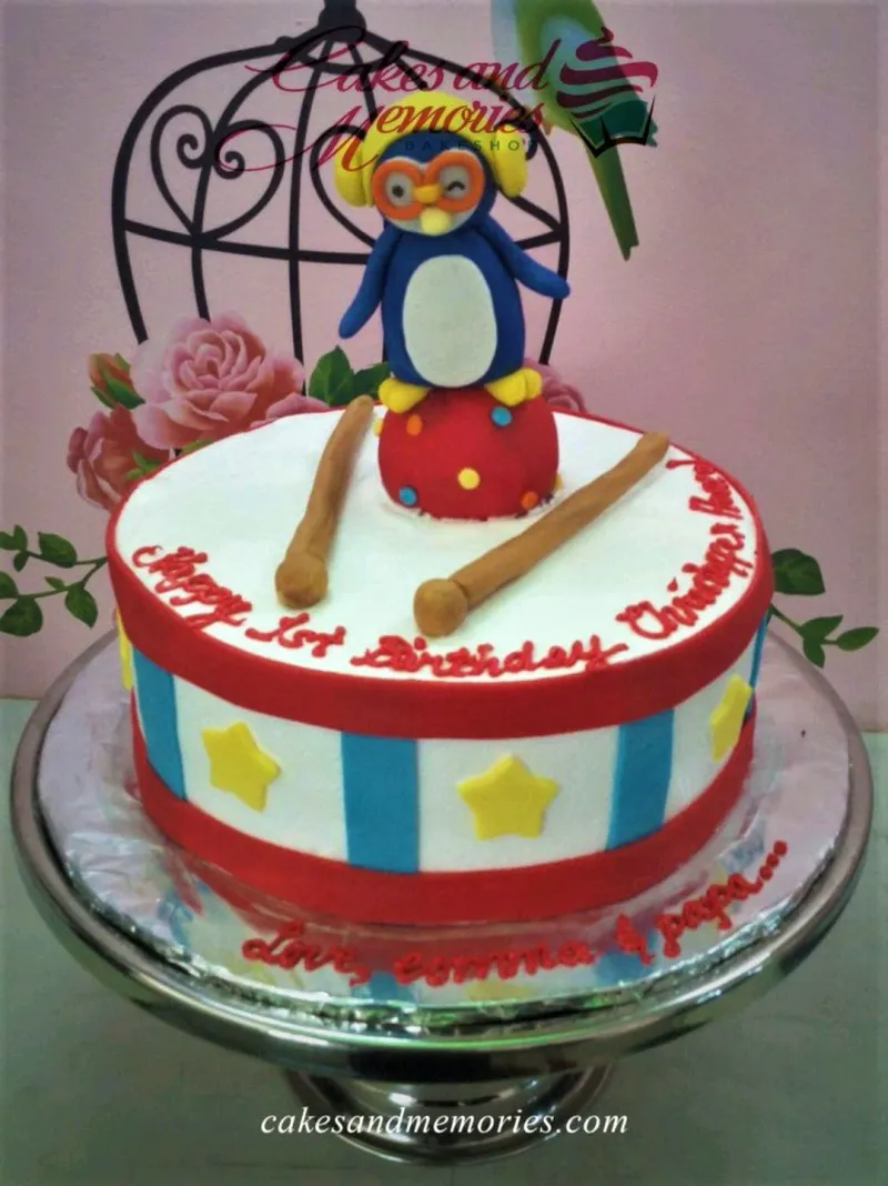 A multicolor 1 Tier Fondant cake themed around Pororo Penguin, featuring a Pororo figure, drumsticks, and stripes. A multicolor 1 Tier Fondant cake themed around Pororo Penguin, featuring a Pororo figure, drumsticks, and stripes.