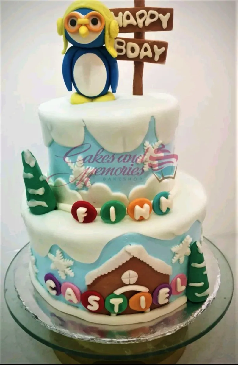 A blue and white two-tier Pororo Penguin fondant cake with a Pororo figure, 'happy bday' sign, snow-like icing, and personalized names. A blue and white two-tier Pororo Penguin fondant cake with a Pororo figure, 'happy bday' sign, snow-like icing, and personalized names.