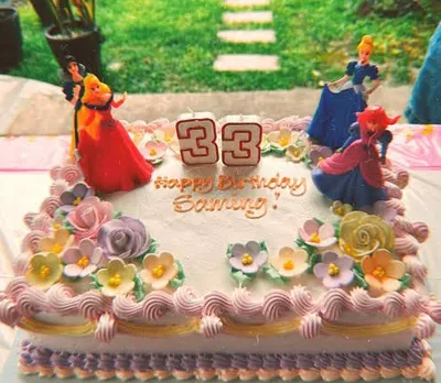 White rectangular soft icing birthday cake decorated with plastic princess figurines number candles and pastel sugar flowers White rectangular soft icing birthday cake decorated with plastic princess figurines number candles and pastel sugar flowers