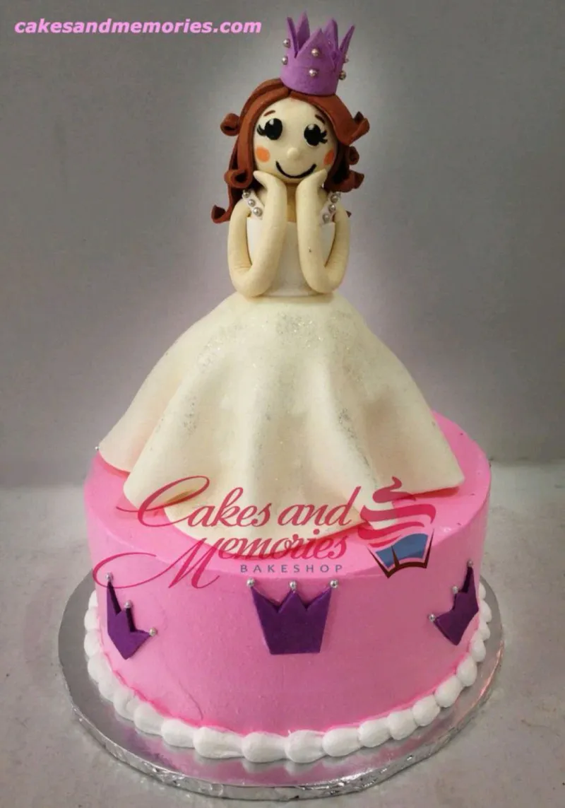 A pink 1-Tier cake themed Princess Doll, featuring a doll topper with white gown and purple crown accents. A pink 1-Tier cake themed Princess Doll, featuring a doll topper with white gown and purple crown accents.