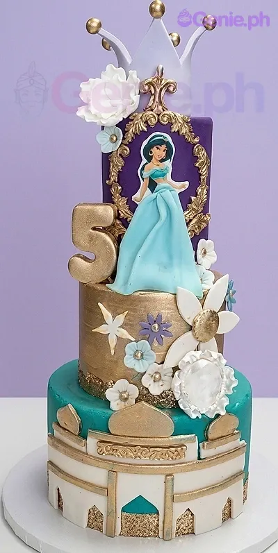 A teal, gold, purple three-tier Princess Jasmine cake with a white crown, character printout, and gold number 5. A teal, gold, purple three-tier Princess Jasmine cake with a white crown, character printout, and gold number 5.