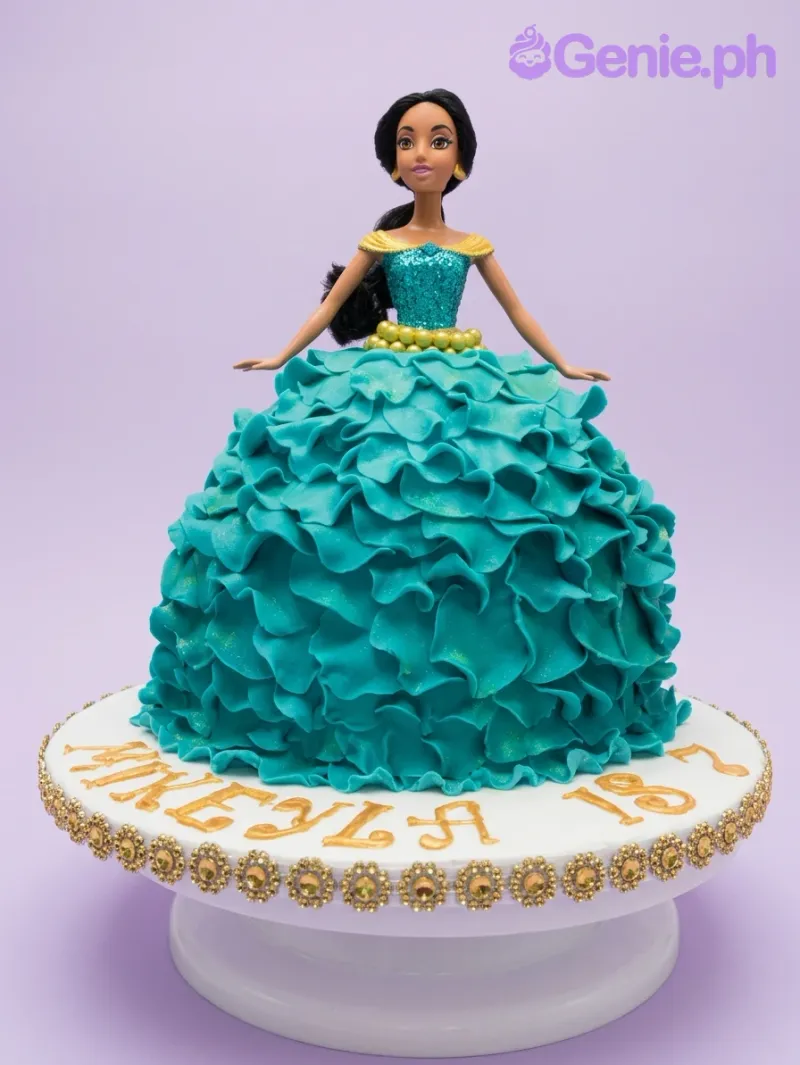 A white and teal Princess Jasmine doll cake with a ruffled gown, gold pearl accents, and "MIKEYLA IS 7" text. A white and teal Princess Jasmine doll cake with a ruffled gown, gold pearl accents, and "MIKEYLA IS 7" text.