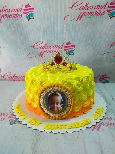 Yellow and orange rosette cake with a gold tiara and a photo printout of a baby girl in the center. Yellow and orange rosette cake with a gold tiara and a photo printout of a baby girl in the center.