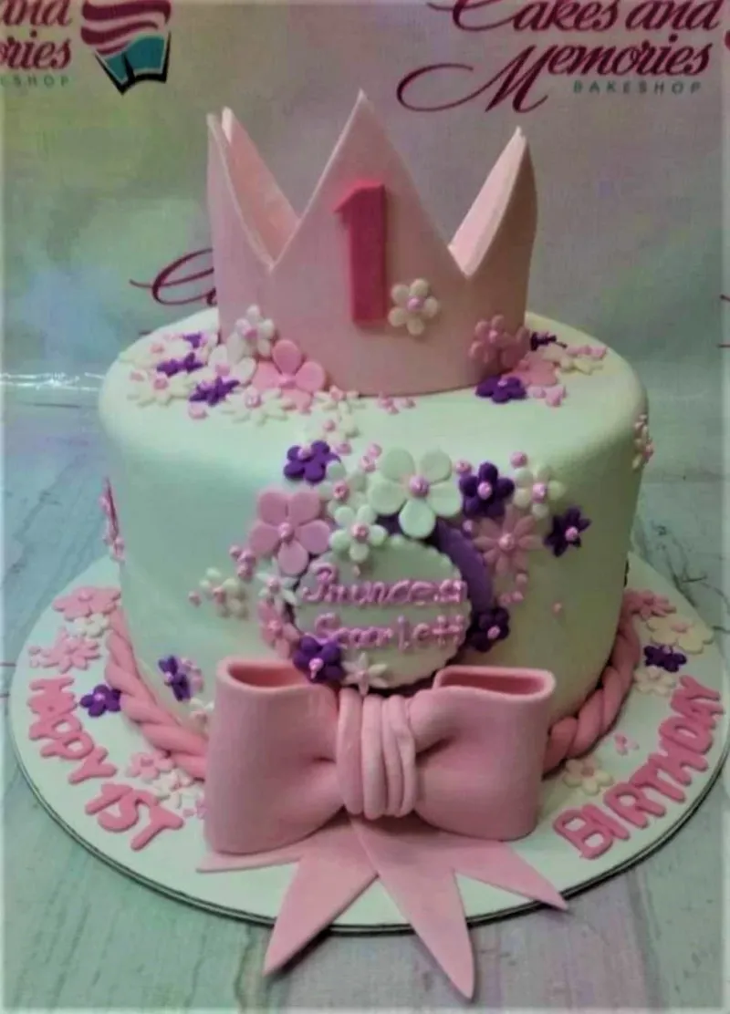 Pink and white princess themed 1st birthday cake with a large fondant crown, pink bow, and purple and pink flowers. Pink and white princess themed 1st birthday cake with a large fondant crown, pink bow, and purple and pink flowers.