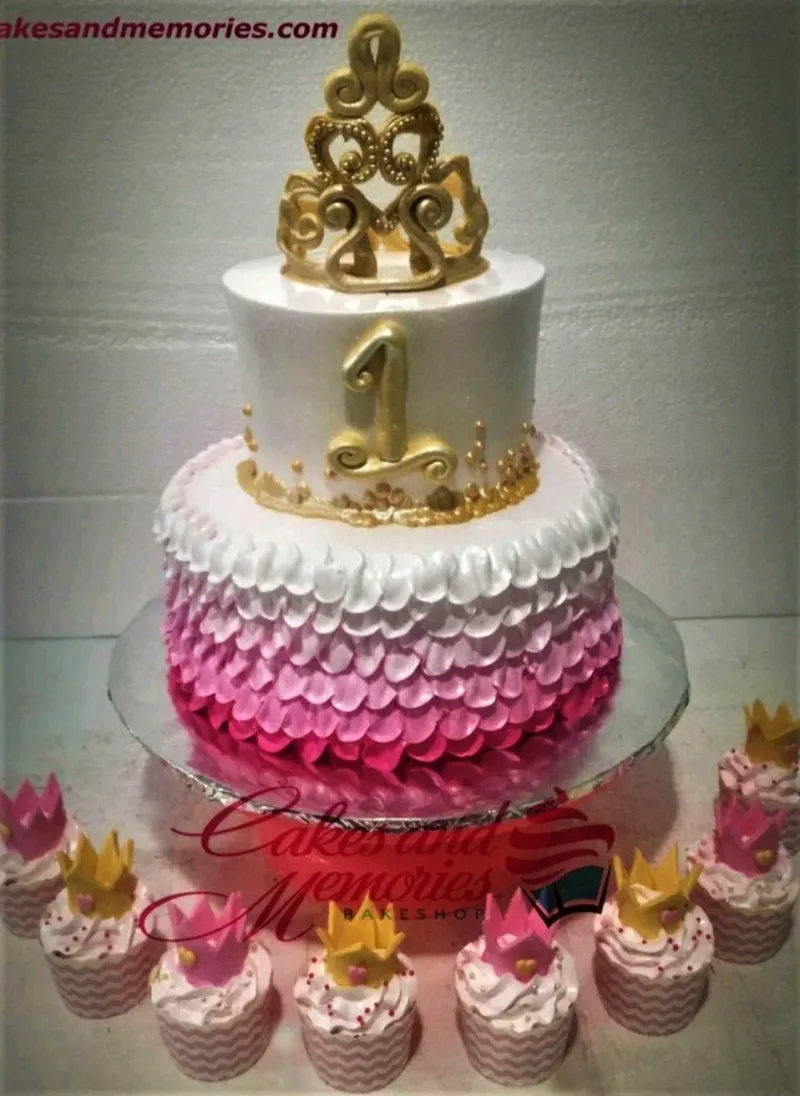 Two-tier pink and white ombre cake with a gold crown topper and gold number one, featuring pink petal-style icing ruffles. Two-tier pink and white ombre cake with a gold crown topper and gold number one, featuring pink petal-style icing ruffles.