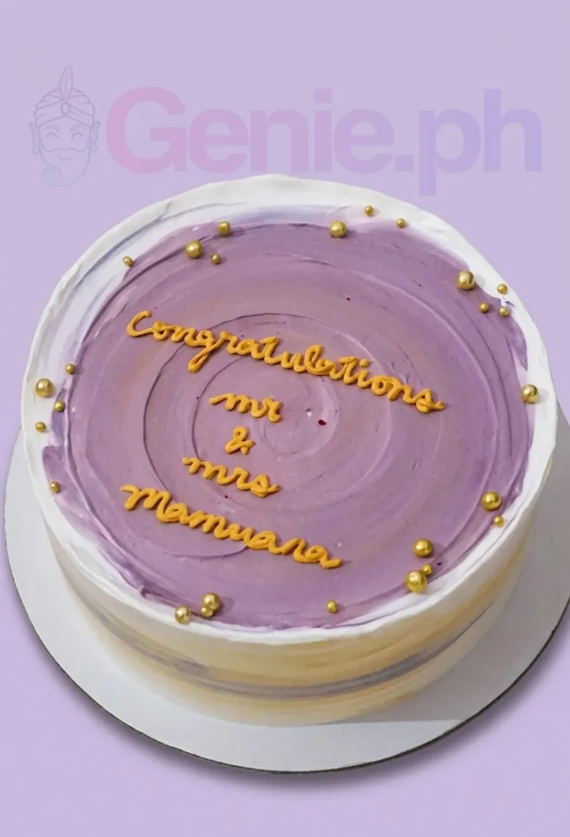 A round, 1-tier purple and white anniversary cake with gold dragees and a yellow icing message. A round, 1-tier purple and white anniversary cake with gold dragees and a yellow icing message.