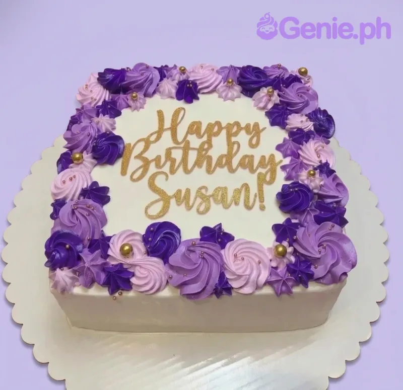 A white square cake with purple and lavender rosettes, gold pearls, and a gold 'Happy Birthday Susan' topper. A white square cake with purple and lavender rosettes, gold pearls, and a gold 'Happy Birthday Susan' topper.