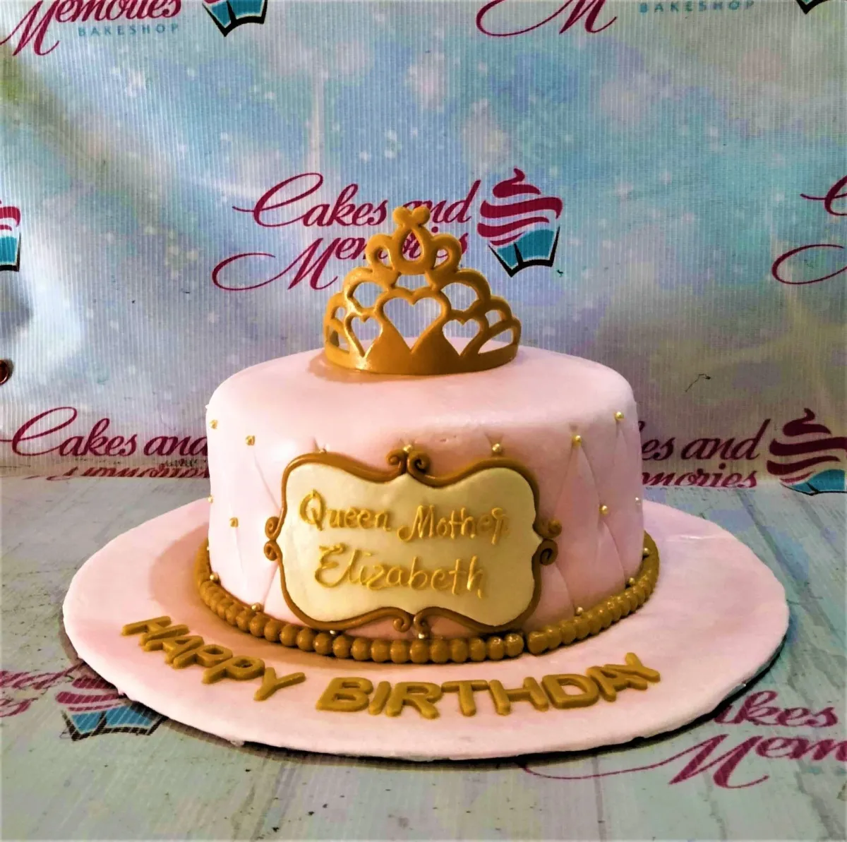 Pink fondant birthday cake for Queen Mother Elizabeth featuring a gold crown toy topper and quilted icing pattern with gold pearls. Pink fondant birthday cake for Queen Mother Elizabeth featuring a gold crown toy topper and quilted icing pattern with gold pearls.