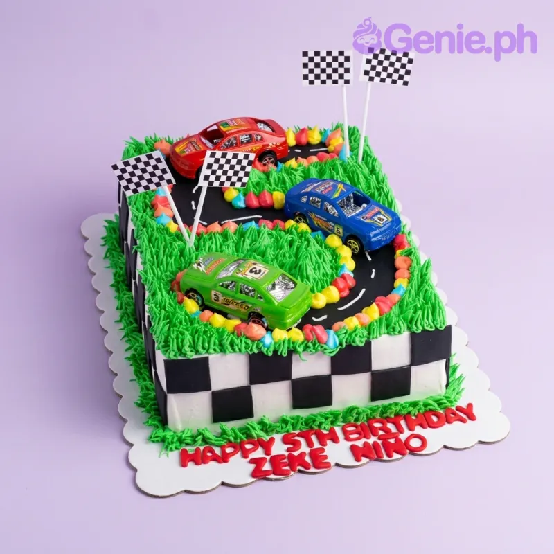 Race car themed rectangle cake with green grass icing, a black racetrack, and three toy cars in red, blue, and green. Race car themed rectangle cake with green grass icing, a black racetrack, and three toy cars in red, blue, and green.