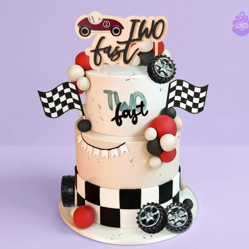 White 2-tier race car themed cake with Two Fast topper and checkered flag decorations White 2-tier race car themed cake with Two Fast topper and checkered flag decorations