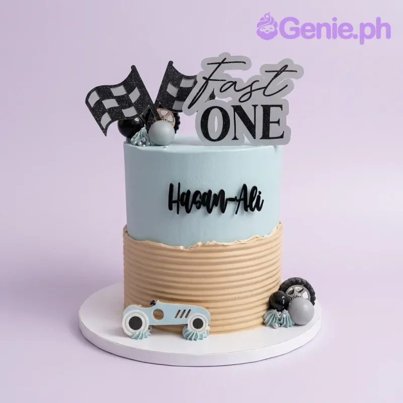 A light blue and tan 1-tier Racing Car cake, featuring 'Fast One' topper, checkered flags, a blue race car, and decorative spheres. A light blue and tan 1-tier Racing Car cake, featuring 'Fast One' topper, checkered flags, a blue race car, and decorative spheres.