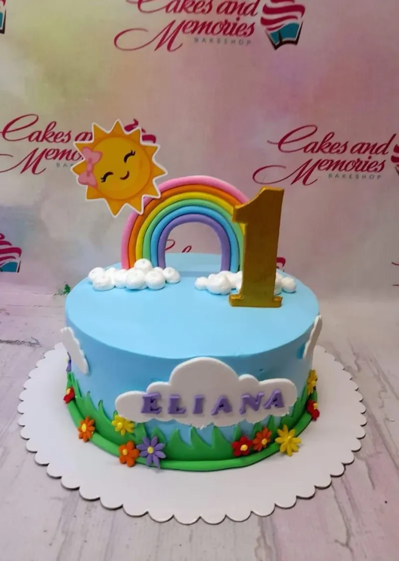 A light blue 1-tier cake themed around a rainbow, featuring a 3D rainbow, smiling sun, gold number one, and white clouds. A light blue 1-tier cake themed around a rainbow, featuring a 3D rainbow, smiling sun, gold number one, and white clouds.