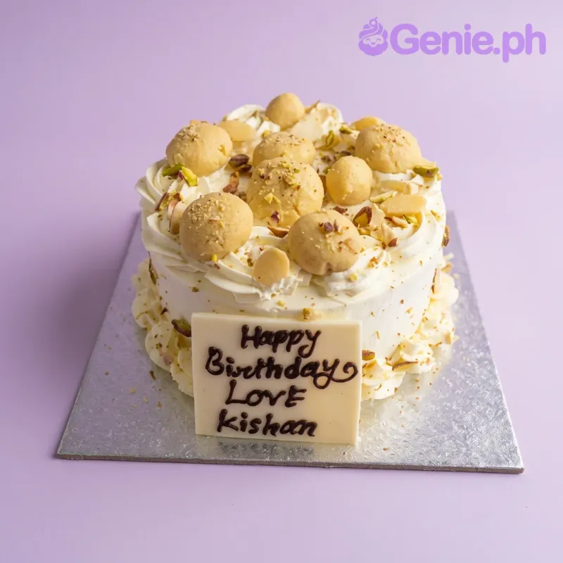 A white soft-icing 1 Tier cake themed around Rasmalai, featuring yellow round sweets, crushed nuts, and a white chocolate message plaque. A white soft-icing 1 Tier cake themed around Rasmalai, featuring yellow round sweets, crushed nuts, and a white chocolate message plaque.
