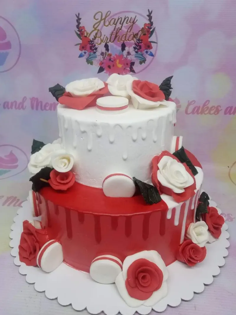 A red and white two-tier cake featuring red and white fondant roses, white macarons, and black fondant leaves. A red and white two-tier cake featuring red and white fondant roses, white macarons, and black fondant leaves.