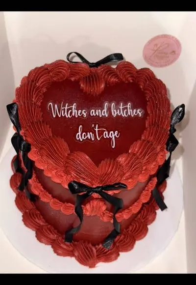Dark red 2-tier vintage cake with soft icing, piped heart rosettes, and black ribbon bows