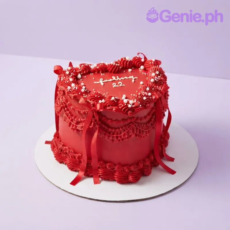 Vibrant red heart cake with smooth soft icing, red satin ribbon bows, and piped red rosettes