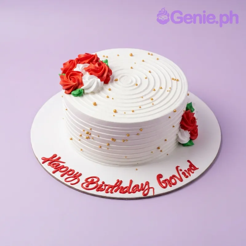 White round cake with red and white icing roses, gold dragees, and a Happy Birthday Govind message on the base board. White round cake with red and white icing roses, gold dragees, and a Happy Birthday Govind message on the base board.