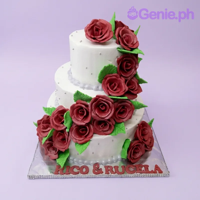 A White 3-tier cake themed for a Red Rose Wedding, featuring cascading deep red gumpaste roses, green leaves, on a silver board. A White 3-tier cake themed for a Red Rose Wedding, featuring cascading deep red gumpaste roses, green leaves, on a silver board.
