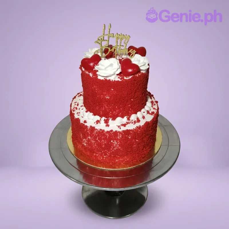 A white, red, and gold 2-tier cake themed around Red Velvet, featuring a gold Happy Birthday topper and red heart toppers, accented with white icing rosettes. A white, red, and gold 2-tier cake themed around Red Velvet, featuring a gold Happy Birthday topper and red heart toppers, accented with white icing rosettes.